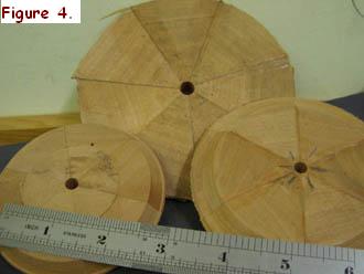 These triangular “pie slices” (which will be cut out later to make a ring of felloes), have been glued together and then held in place on a board using nails and tapered chocks to hold everything in place whilst the glue dries.